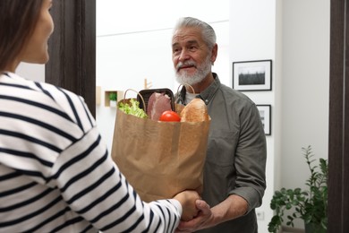 Photo of Courier giving paper bag with food products to senior man indoors