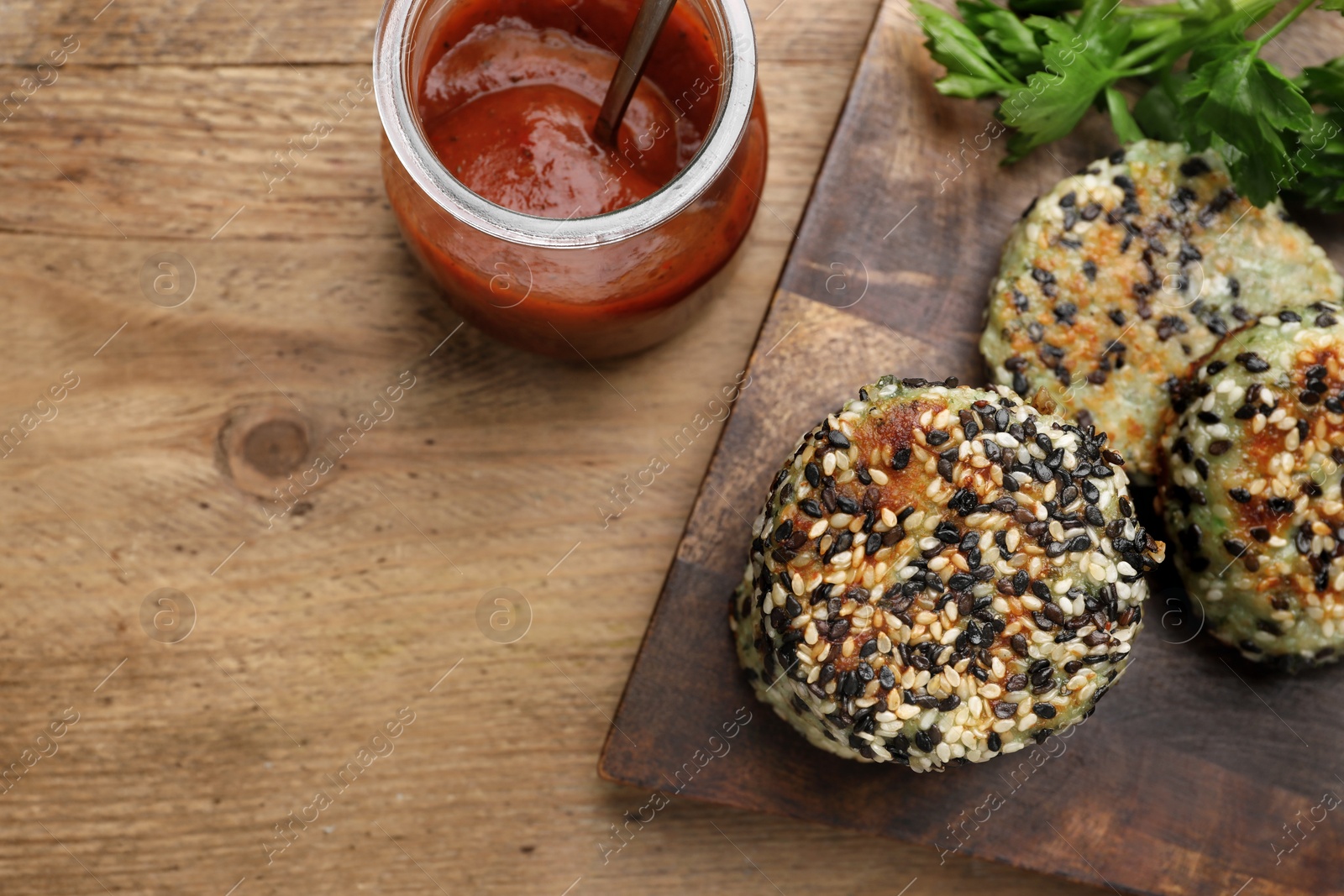 Photo of Delicious vegan cutlets with sesame , ketchup and parsley on wooden table, above view