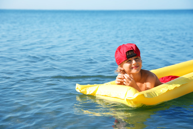 Cute little child with mattress in sea on sunny day. Beach holiday