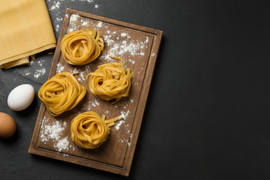 Raw tagliatelle pasta and products on black table, flat lay. Space for text