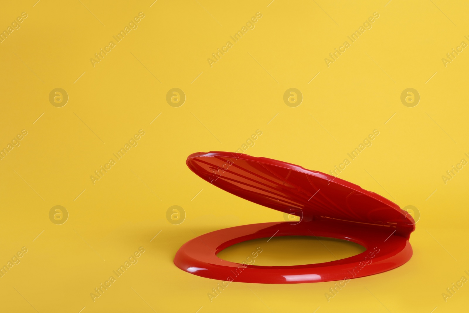 Photo of New red plastic toilet seat on yellow background, space for text