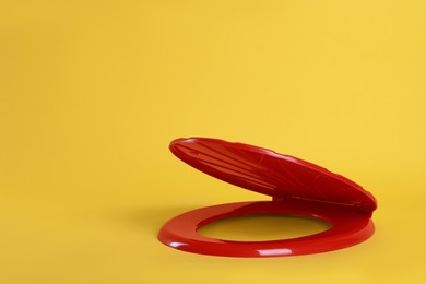 Photo of New red plastic toilet seat on yellow background, space for text