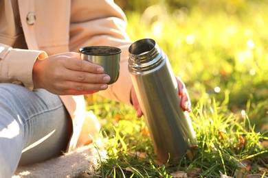 Photo of Woman with thermos and cup lid on green grass outdoors, closeup. Space for text