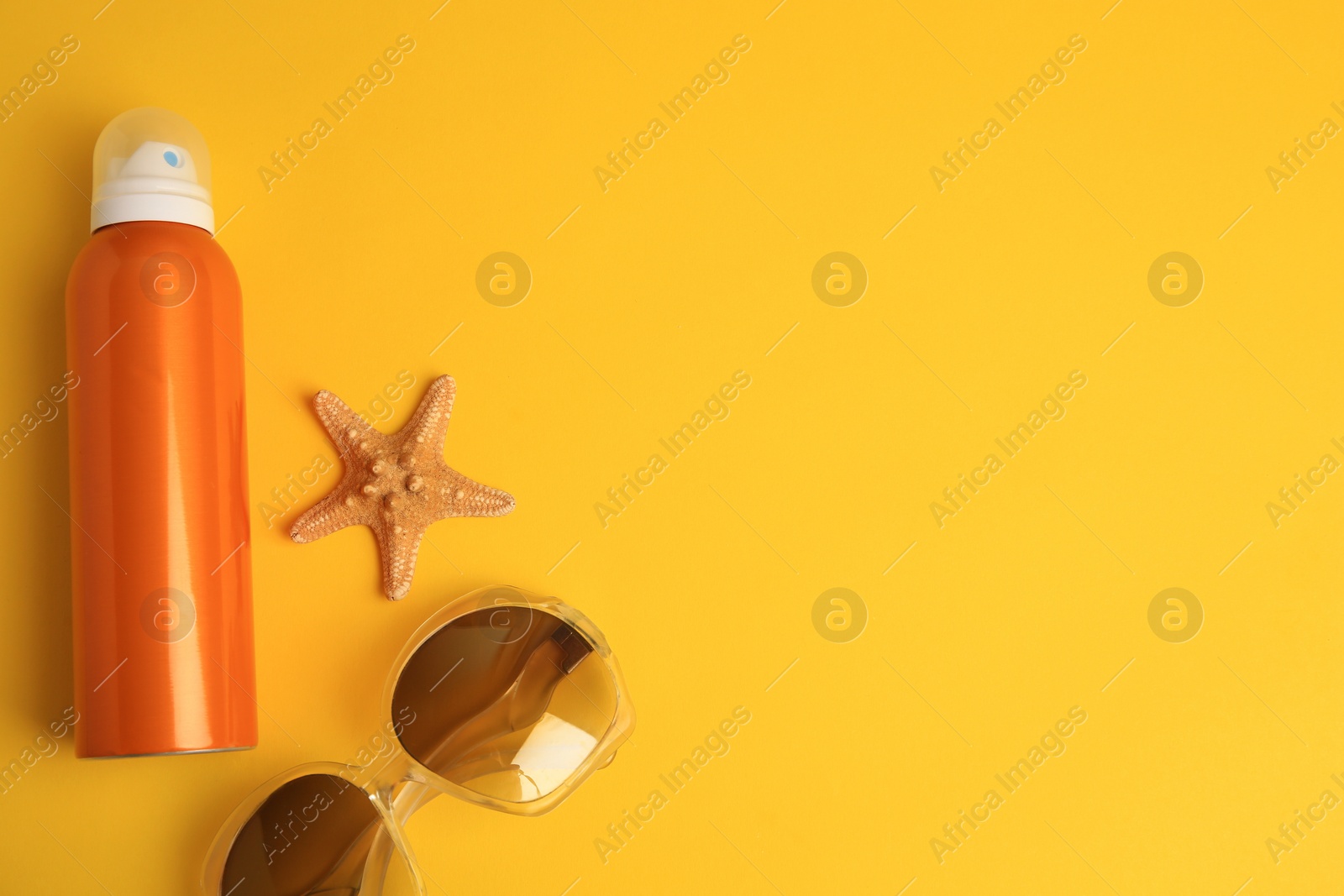 Photo of Bottle of sunscreen, starfish and sunglasses on yellow background, flat lay. Space for text