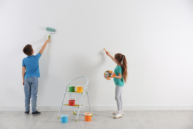 Little children painting on blank white wall indoors