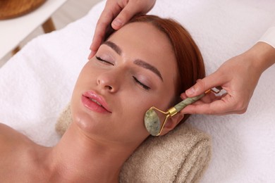 Photo of Young woman receiving facial massage with jade roller in beauty salon, above view