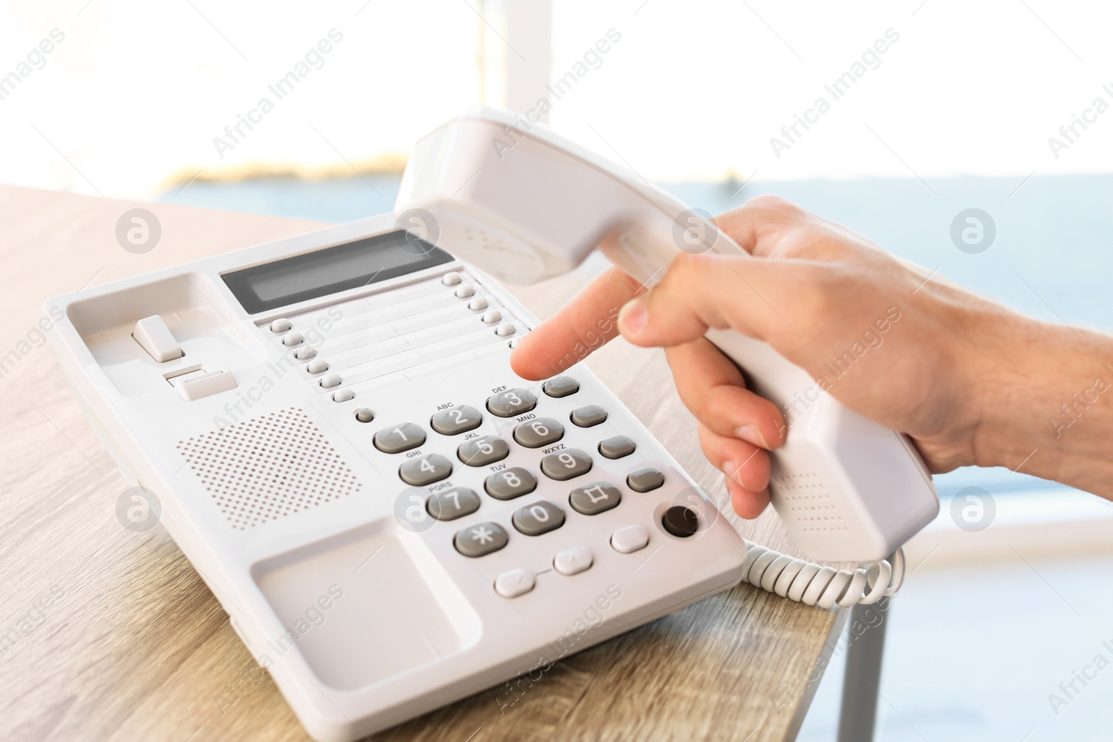 Photo of Man dialing number on telephone at table indoors