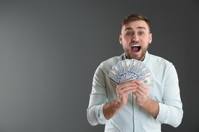 Portrait of emotional young man with money on grey background. Space for text