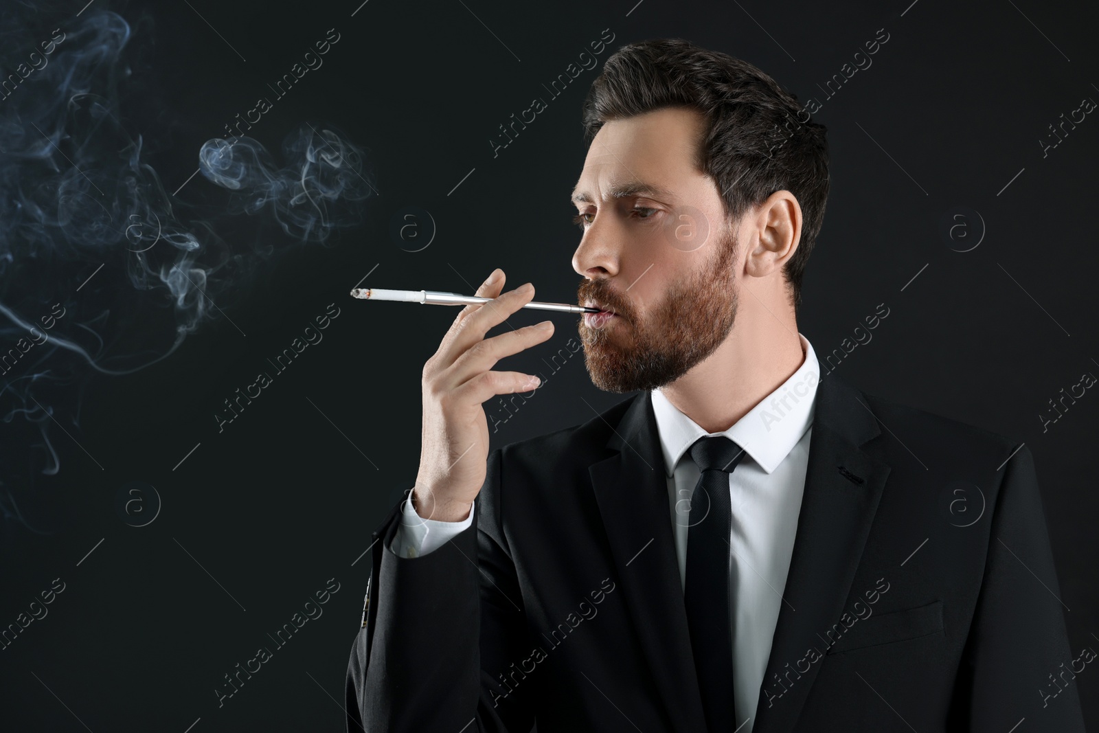Photo of Man using long cigarette holder for smoking on black background