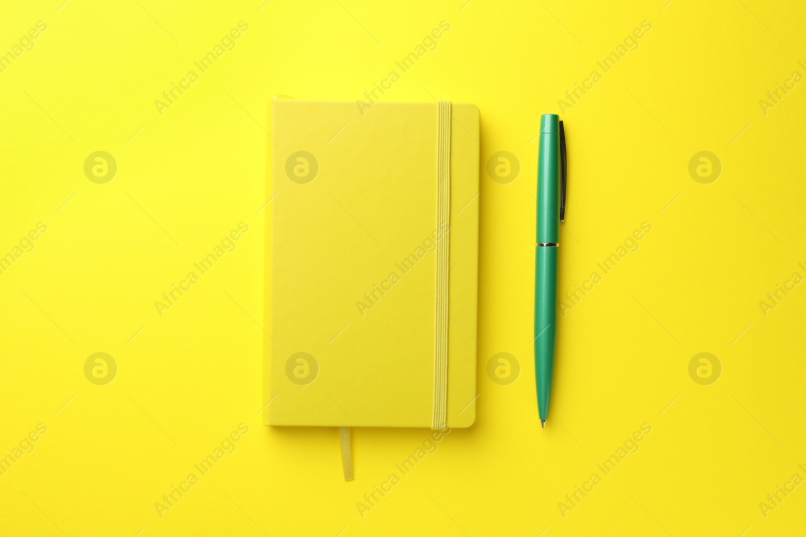 Photo of Closed notebook and pen on yellow background, top view