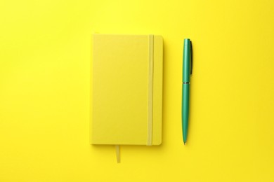 Photo of Closed notebook and pen on yellow background, top view