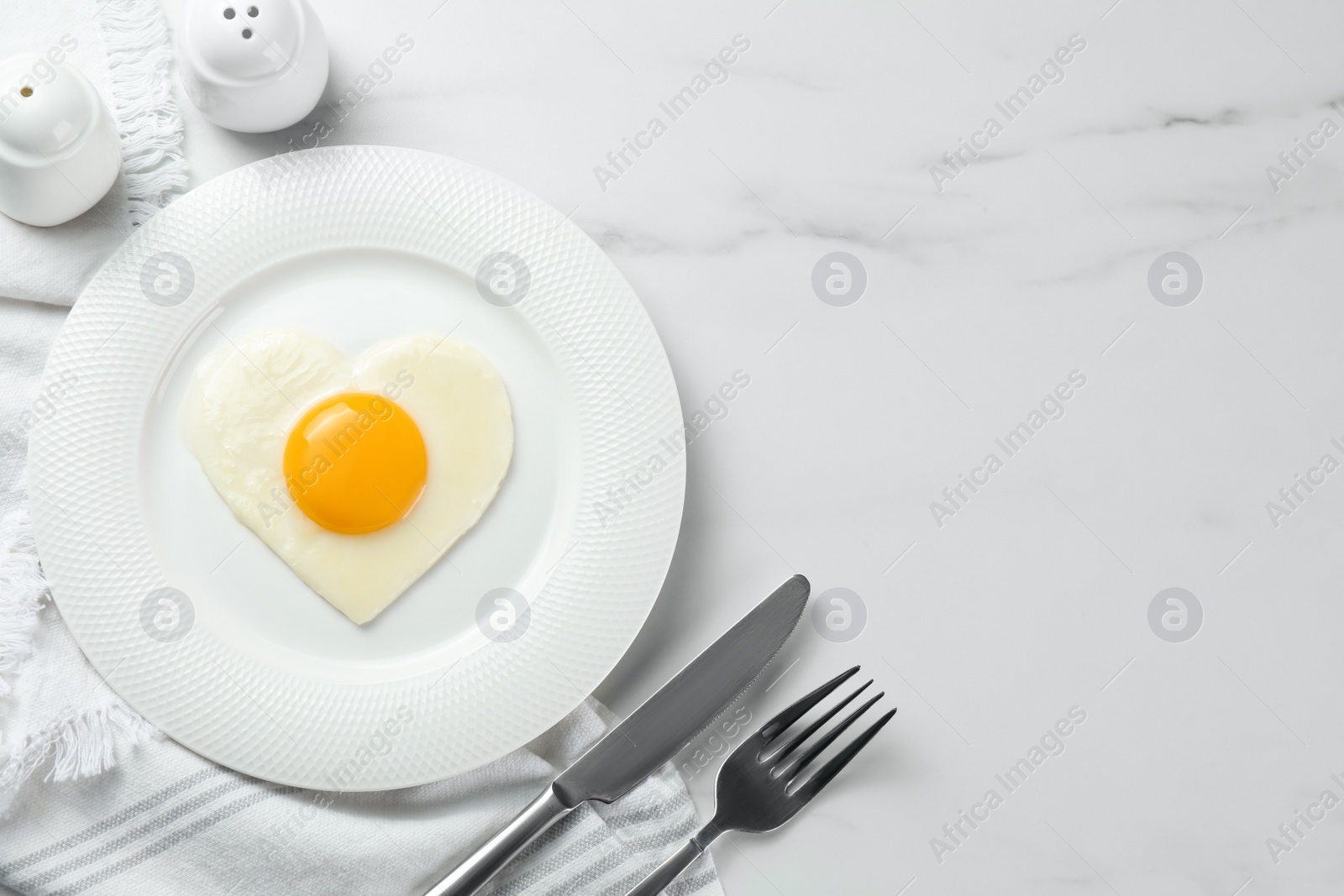 Photo of Heart shaped fried egg served on white marble table, flat lay. Space for text