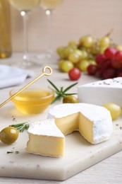 Photo of Tasty brie cheese with olives and rosemary on white board
