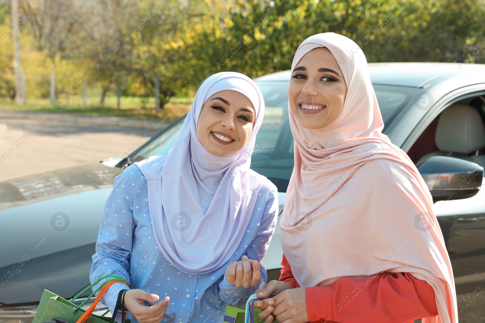 Photo of Muslim women with shopping bags near car outdoors
