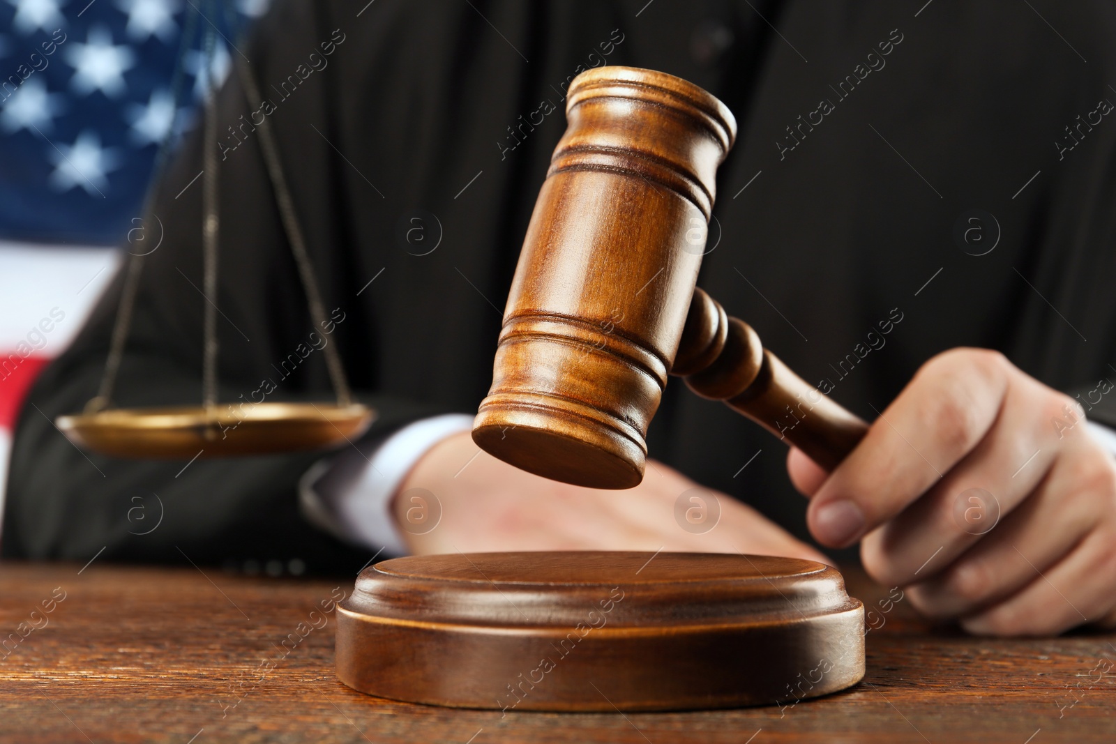 Photo of Judge with gavel at wooden table near flag of United States, closeup