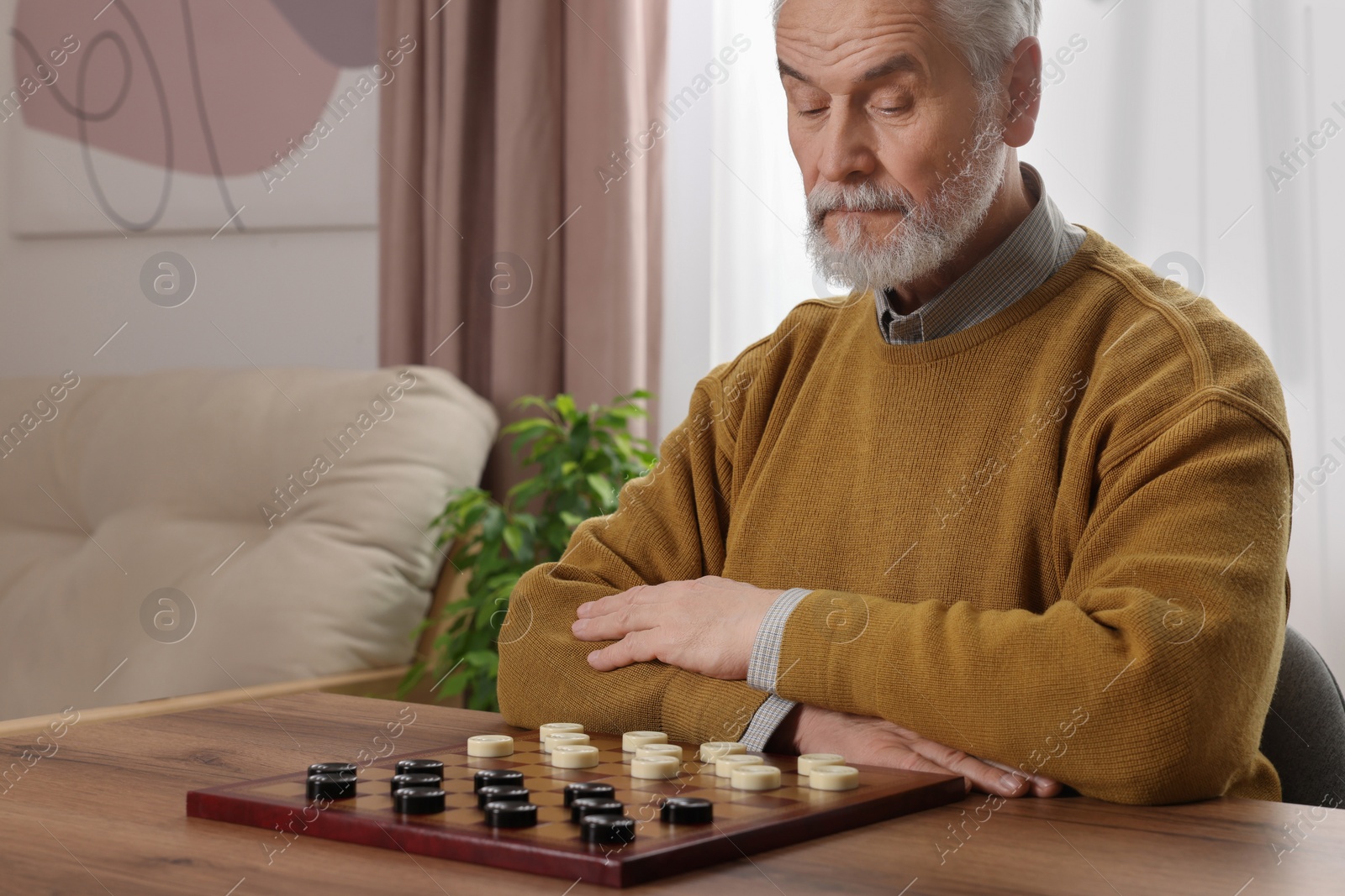 Photo of Playing checkers. Concentrated senior man thinking about next move at table in room