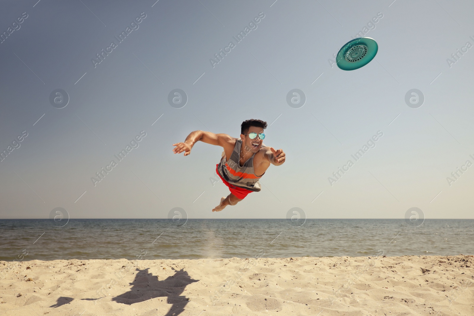 Photo of Sportive man jumping while trying to catch flying disk at beach