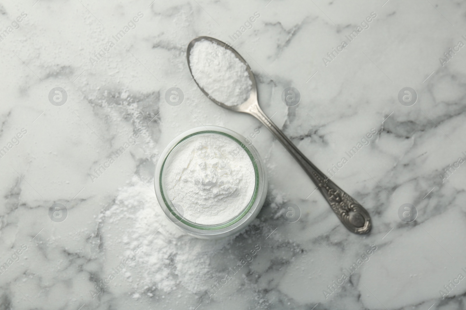 Photo of Baking powder in jar and spoon on white marble table, top view