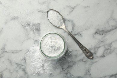 Baking powder in jar and spoon on white marble table, top view