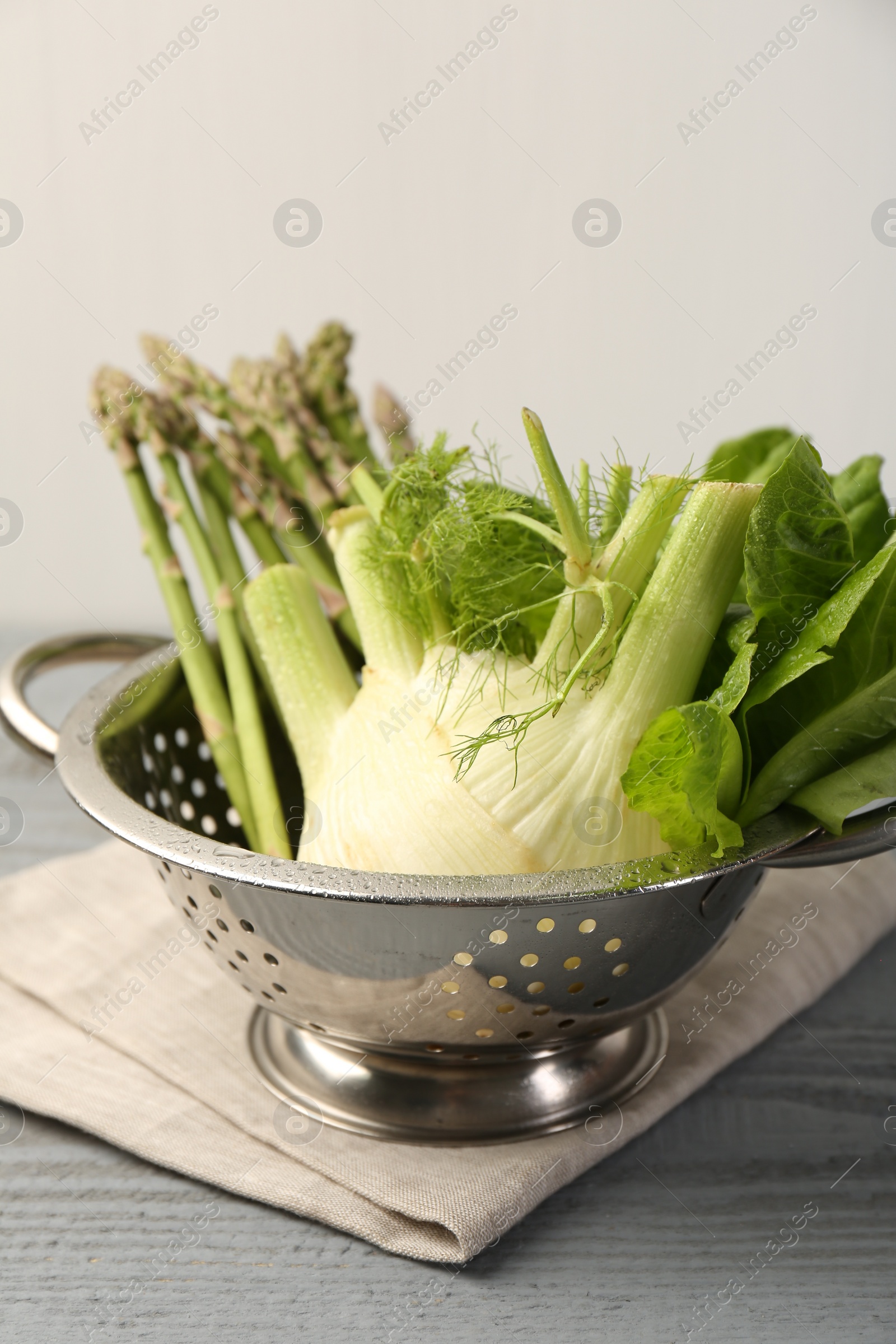 Photo of Metal colander with fennel, lettuce and asparagus on gray wooden table