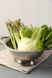 Photo of Metal colander with fennel, lettuce and asparagus on gray wooden table