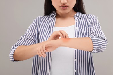 Photo of Suffering from allergy. Young woman scratching her arm on grey background, closeup