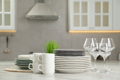 Photo of Clean plates, cups and glasses on white marble table in kitchen