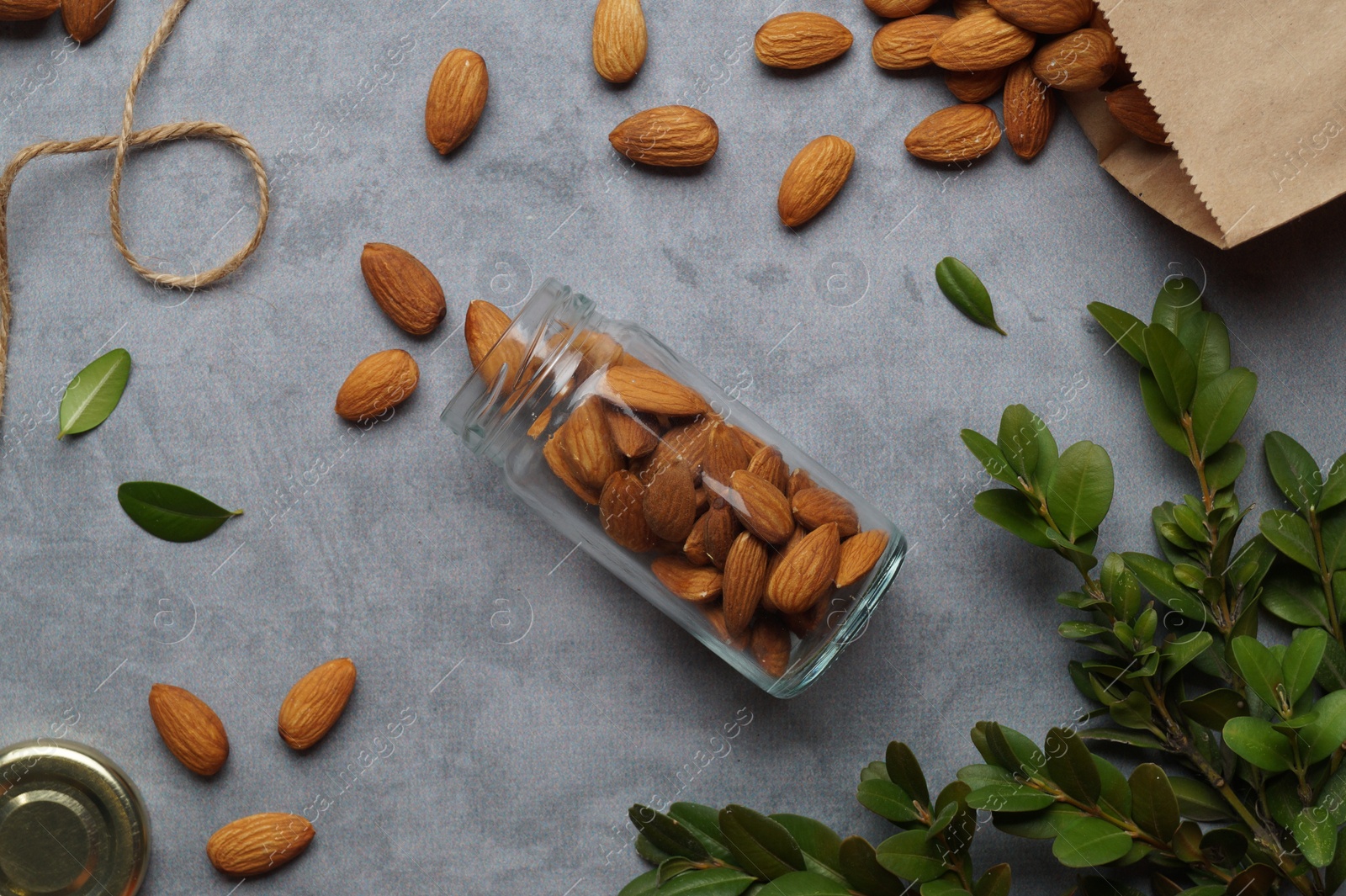 Photo of Jar with tasty almonds and green leaves on light grey table, flat lay