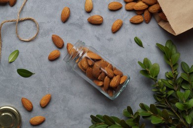 Jar with tasty almonds and green leaves on light grey table, flat lay