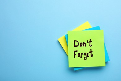 Photo of Paper note with phrase Don't Forget on light blue background, top view. Space for text