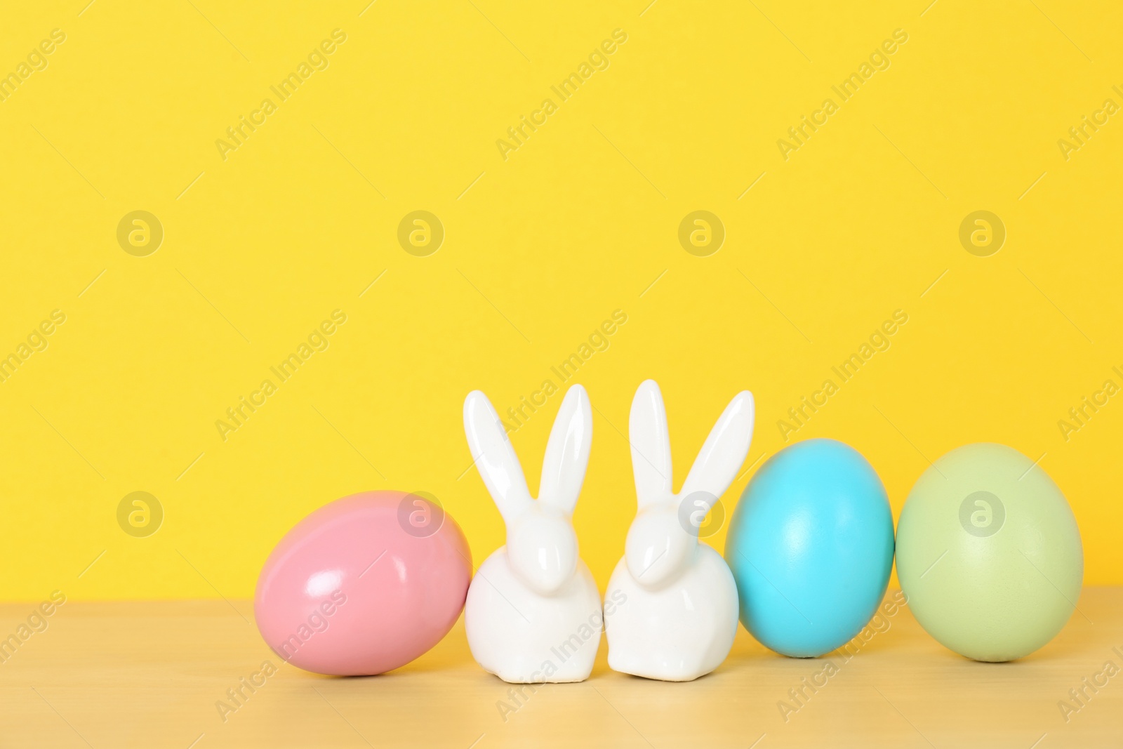 Photo of Cute ceramic Easter bunnies and dyed eggs on table against color background, space for text