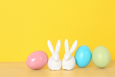 Cute ceramic Easter bunnies and dyed eggs on table against color background, space for text