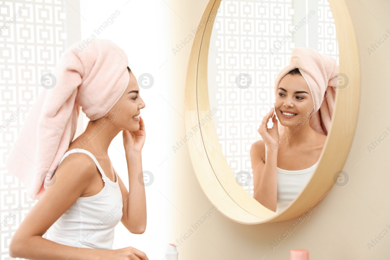 Photo of Pretty young woman with towel on head near mirror in bathroom