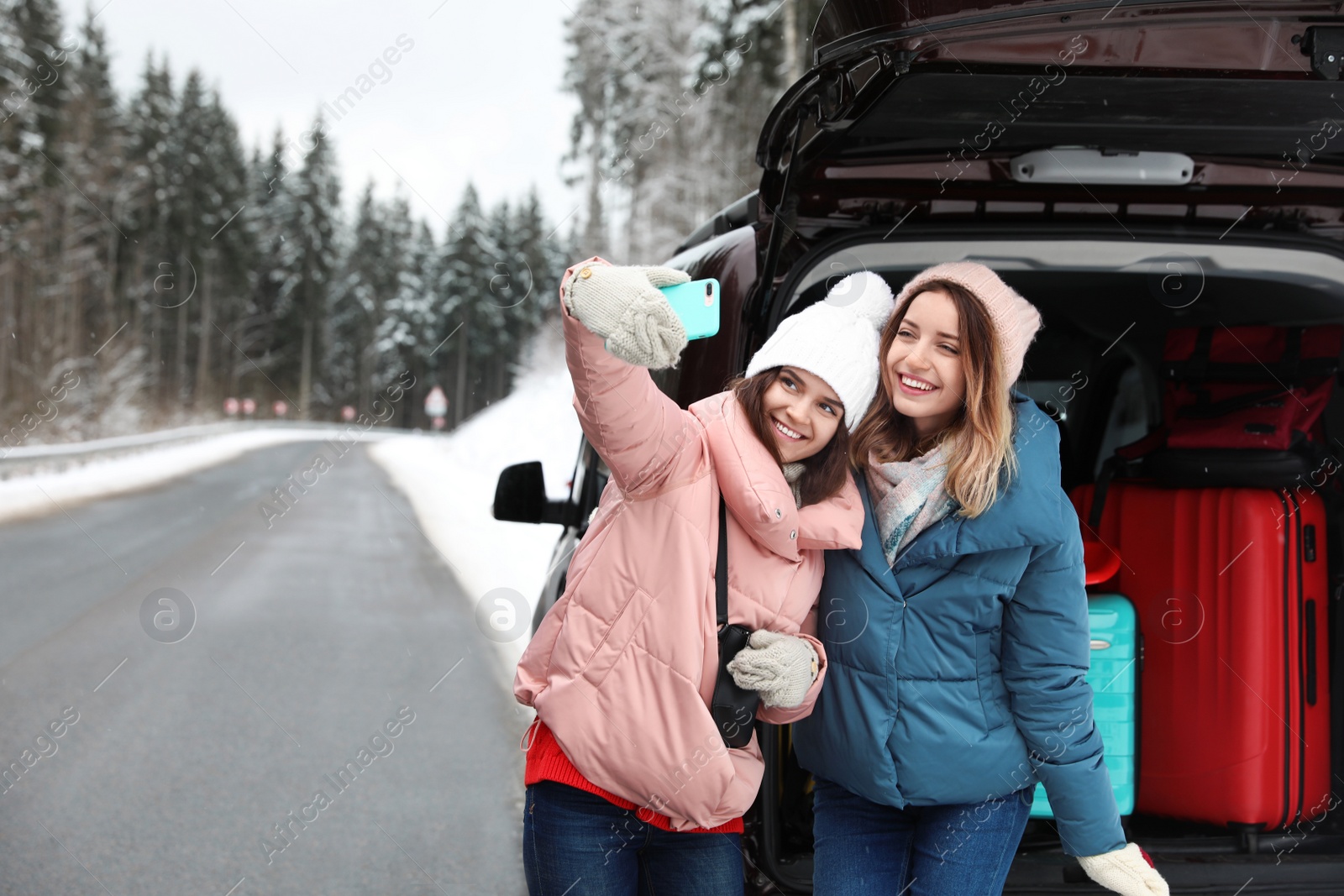 Photo of Friends taking selfie near open car trunk full of luggage on road, space for text. Winter vacation