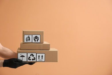 Courier holding cardboard boxes with different packaging symbols on orange background, space for text. Parcel delivery