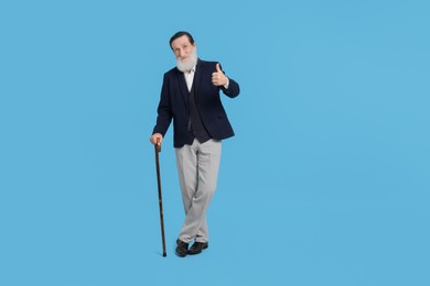Photo of Senior man with walking cane showing thumb up on light blue background