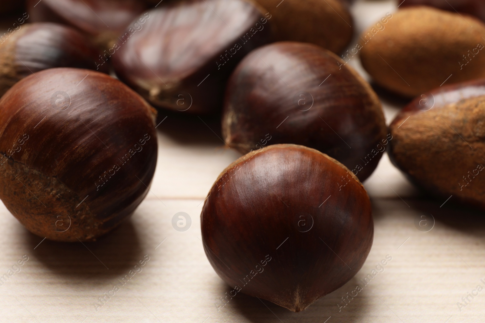 Photo of Sweet fresh edible chestnuts on light wooden table, closeup