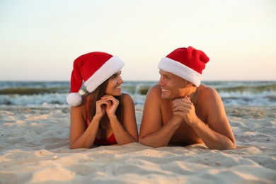 Photo of Happy couple with Santa hats together on beach. Christmas vacation