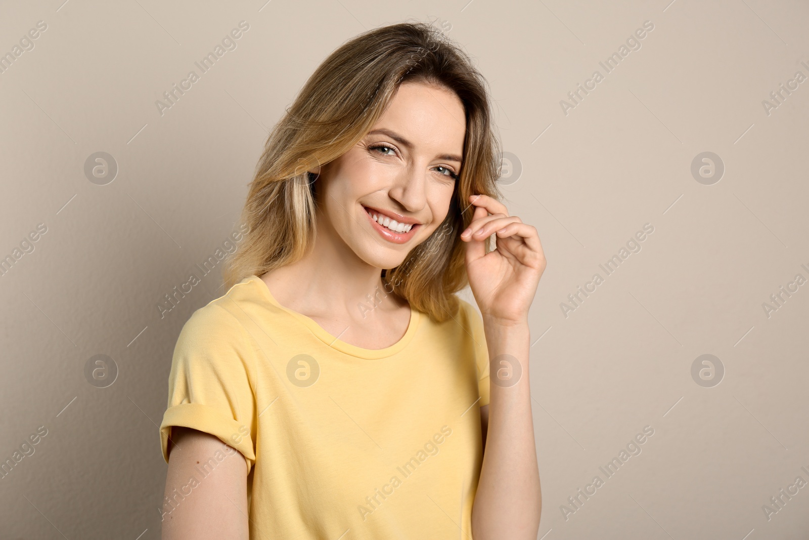 Photo of Portrait of happy young woman with beautiful blonde hair and charming smile on beige background