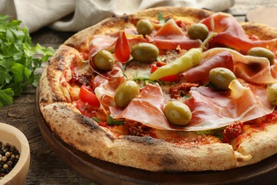 Photo of Tasty pizza with cured ham, olives, sun-dried tomato and pepper on wooden table, closeup