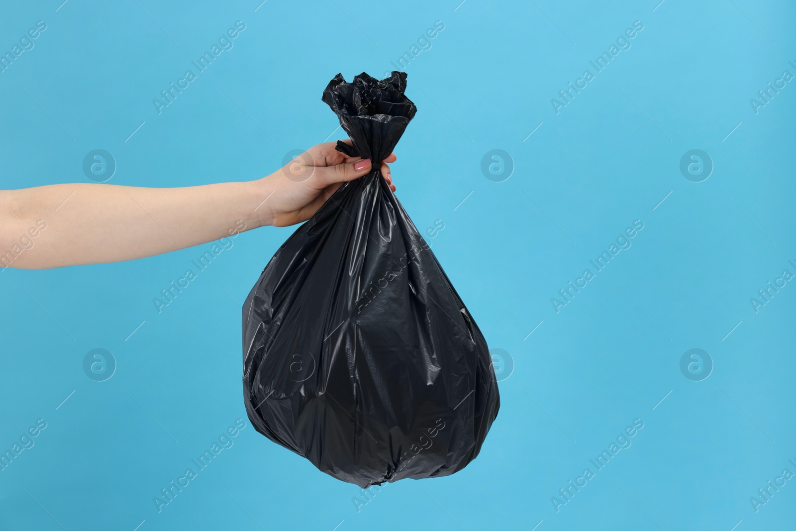 Photo of Woman holding plastic bag full of garbage on light blue background, closeup. Space for text