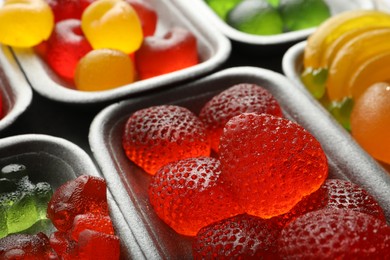 Different delicious gummy candies in containers, closeup