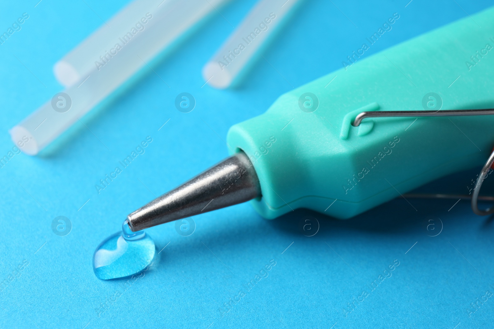 Photo of Melted glue dripping out of hot gun nozzle on light blue background, closeup