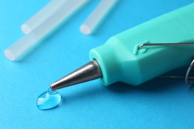 Melted glue dripping out of hot gun nozzle on light blue background, closeup