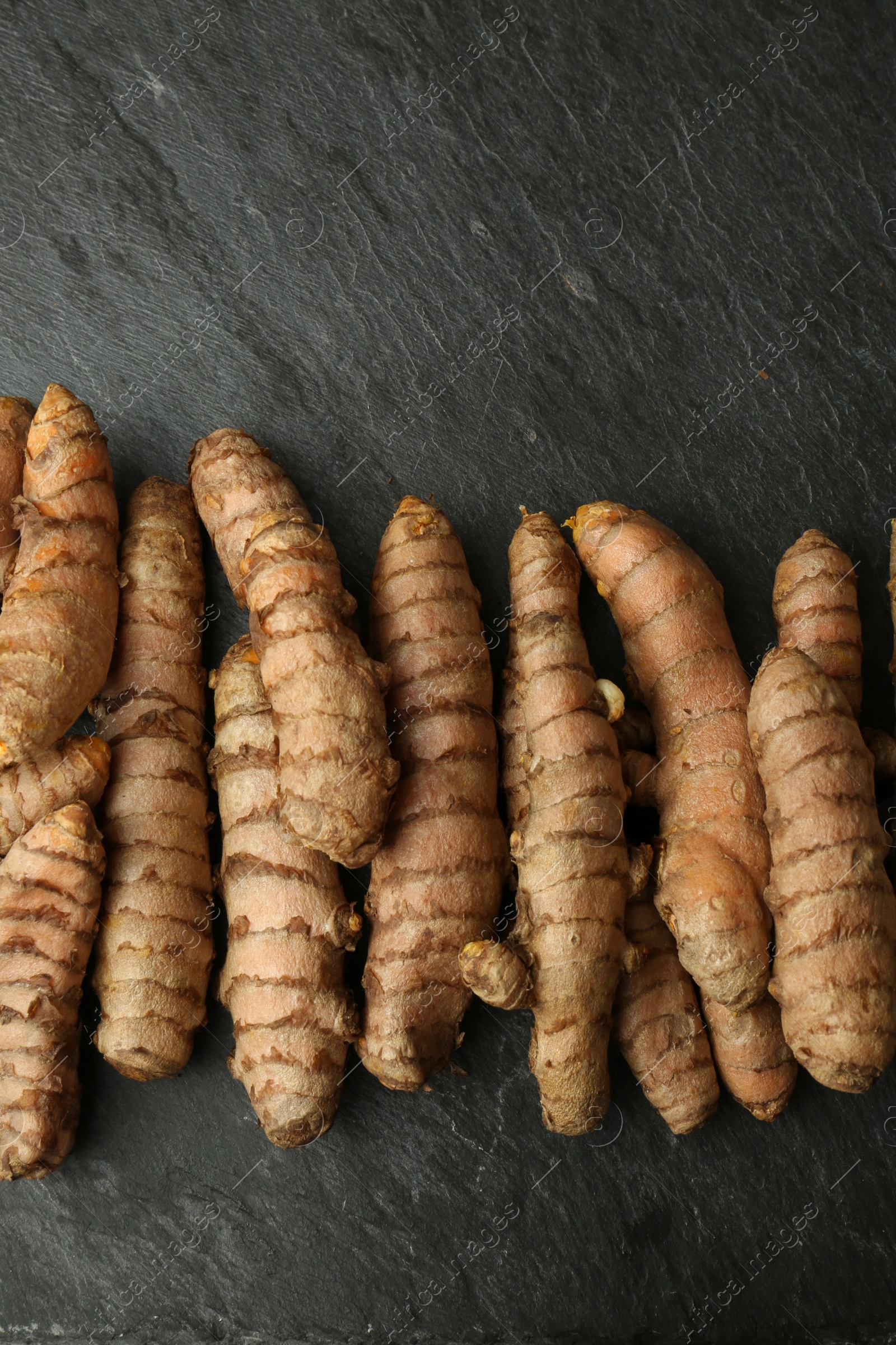 Photo of Many raw turmeric roots on black textured table, flat lay. Space for text