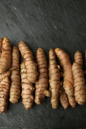 Many raw turmeric roots on black textured table, flat lay. Space for text