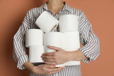 Photo of Woman with heap of toilet paper rolls on brown background, closeup