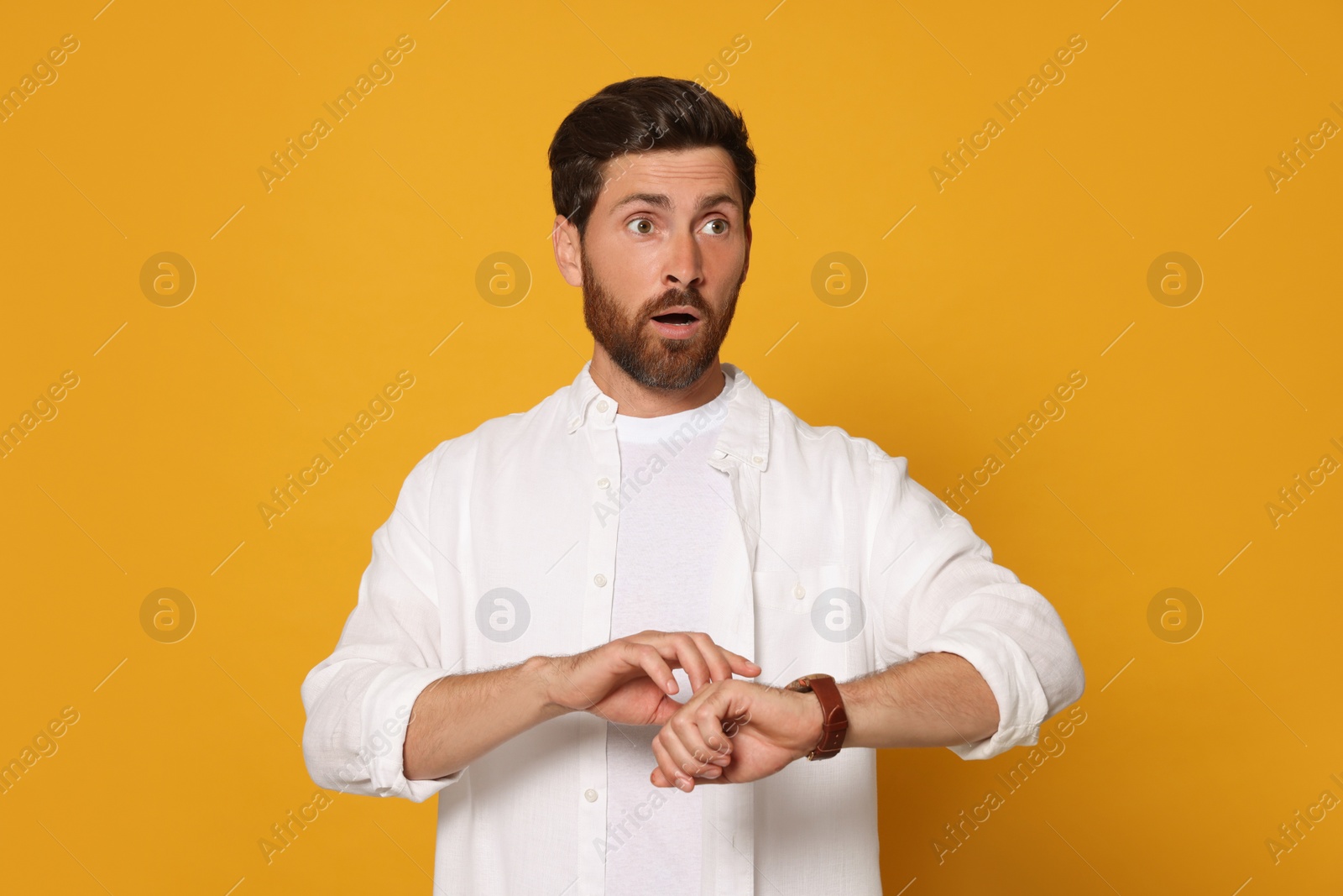 Photo of Emotional man checking time on orange background. Being late concept