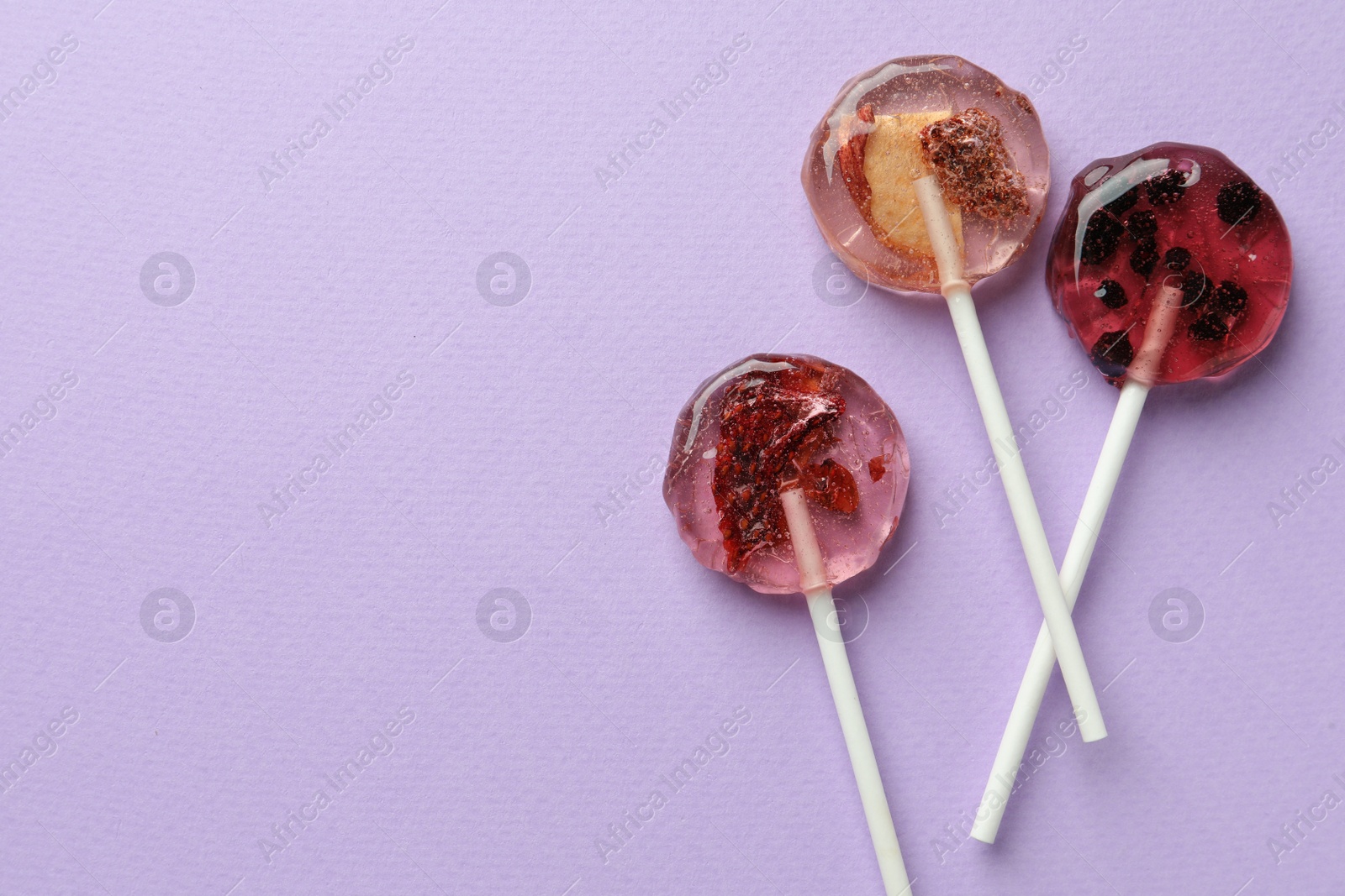 Photo of Sweet colorful lollipops with berries on lilac background, flat lay. Space for text