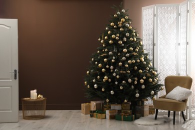 Photo of Beautifully decorated Christmas tree and many gift boxes near brown wall in room